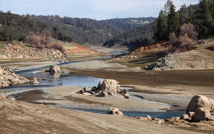 shutterstock_1896379093 Drought-exposed riverbed with scattered boulders and low water