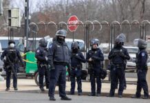 Five Arrests Put A Key Airbase On Alert Group of police officers in riot gear standing on a street; Brian Folkerts present