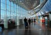 Passengers walk through a modern airport terminal with shops and glass walls
