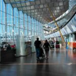 Shots Reported – Traveler Chaos Erupts Passengers walk through a modern airport terminal with shops and glass walls