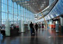 Passengers walk through a modern airport terminal with shops and glass walls