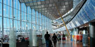 Passengers walk through a modern airport terminal with shops and glass walls