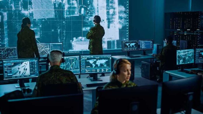 shutterstock_1936992886 Military analysts monitor data on multiple screens in a command center