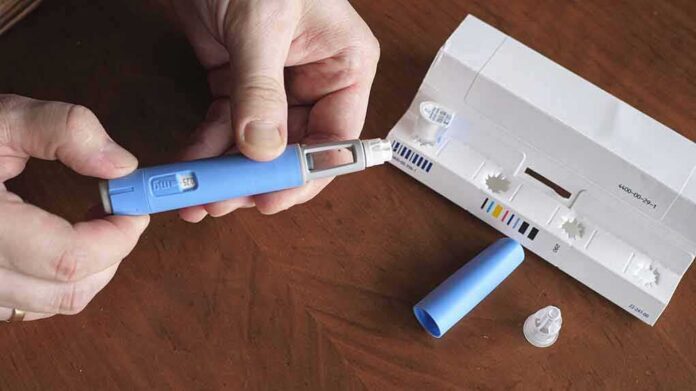 Hands assembling a blue insulin pen with packaging on a table