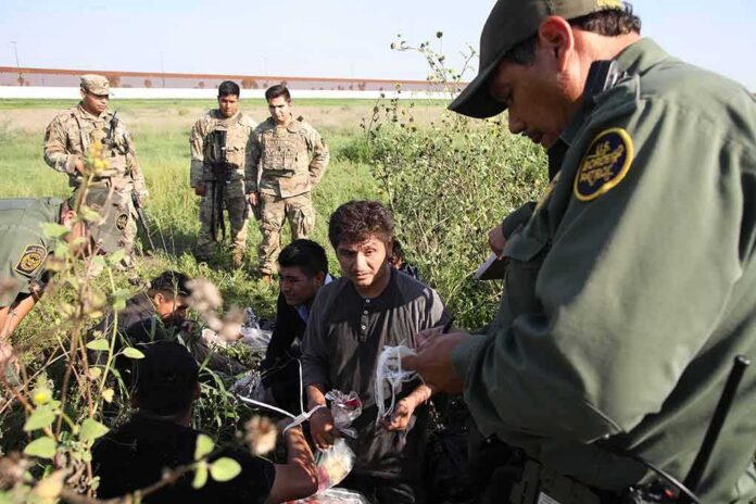 Border agents detain a group of migrants in a grassy field