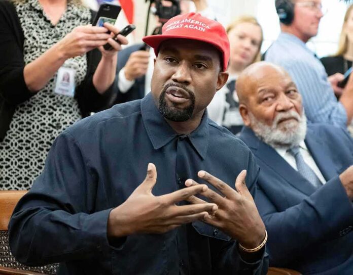 shutterstock_2274977203 Kanye West speaking while Jim Brown sits nearby in a crowded room