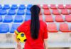 Soccer player in red shirt holding ball in empty stadium seats