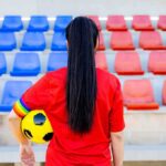Soccer player in red shirt holding ball in empty stadium seats