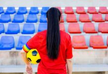 Soccer player in red shirt holding ball in empty stadium seats