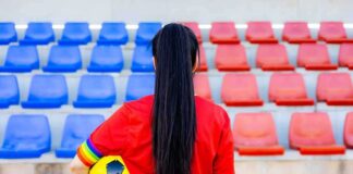 Soccer player in red shirt holding ball in empty stadium seats
