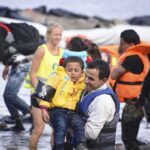 Vacation Nightmare: Boat Explodes Into Flames man carries child wearing life jacket at shoreline