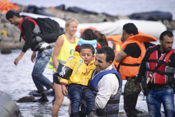 man carries child wearing life jacket at shoreline