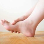 Innocent Sprain? Cancer Was Hiding Hand holding the arch of a bare foot on a wooden floor