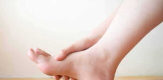 Hand holding the arch of a bare foot on a wooden floor