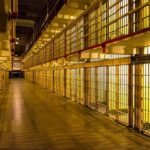 Prison cell block corridor with barred cells and upper walkways