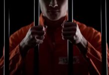 Prisoner in orange jumpsuit gripping jail bars