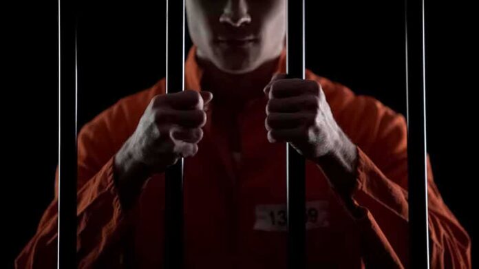 Prisoner in orange jumpsuit gripping jail bars