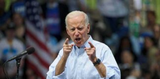 Joe Biden speaking at a rally, pointing with both hands at the podium