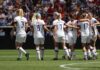 Alex Morgan, Crystal Dunn, Christian Jones, and Walter Jones among teammates celebrating on a soccer field