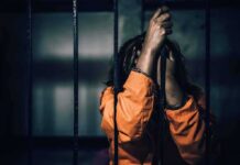 Prisoner in orange jumpsuit gripping jail bars