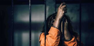 Prisoner in orange jumpsuit gripping jail bars