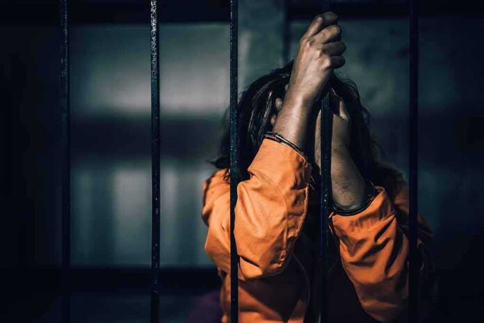 Prisoner in orange jumpsuit gripping jail bars