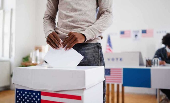 shutterstock_1823718200 Voter places ballot into a box at a polling station
