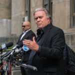 Steve Bannon speaks at a press conference with multiple microphones outside a building