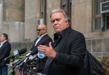 Steve Bannon speaks at a press conference with multiple microphones outside a building