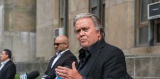 Steve Bannon speaks at a press conference with multiple microphones outside a building