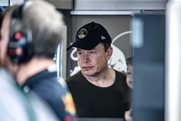 Elon Musk wearing a black cap in a crowded indoor setting