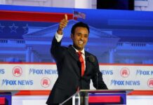 smiling man in suit at debate podium giving thumbs up