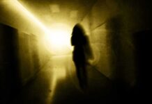 Silhouette of a person in a dim hallway walking toward a bright light