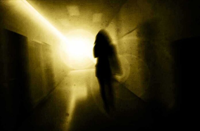 Silhouette of a person in a dim hallway walking toward a bright light
