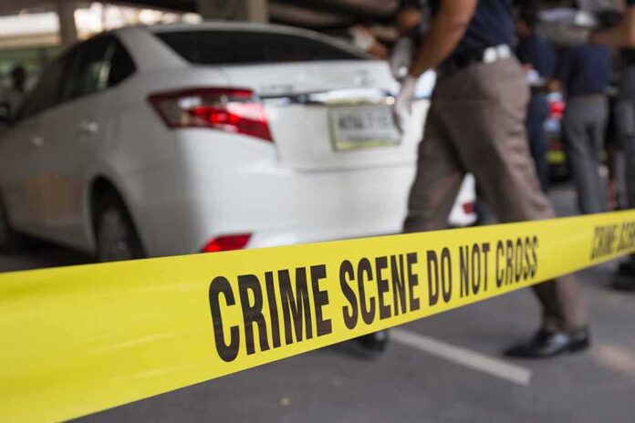 Yellow crime scene tape in front of a white car with investigators nearby