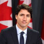 Language Police Drama Grips Trudeau Cabinet man in suit at podium with Canadian flags