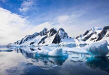 Icebergs floating before snow-covered mountains under a bright sky