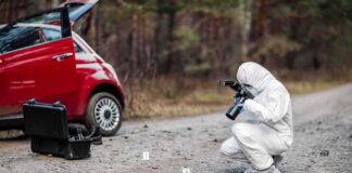 Forensic investigator photographing evidence near a red car on a rural road